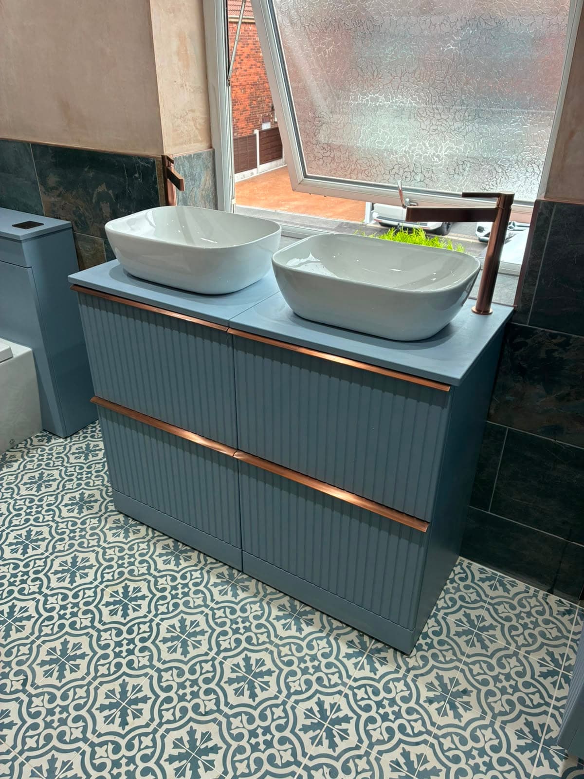 Bathroom with two white countertop basins on a blue-grey fluted double vanity with copper handles, over a blue patterned floor