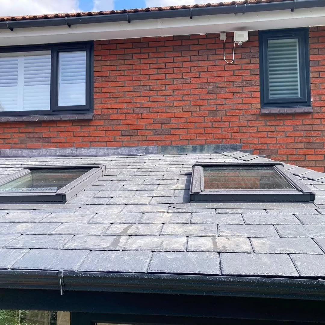 Close view of a completed warm roof in grey lightweight tiles with two Velux roof windows, against the brick wall and shuttered windows of the house